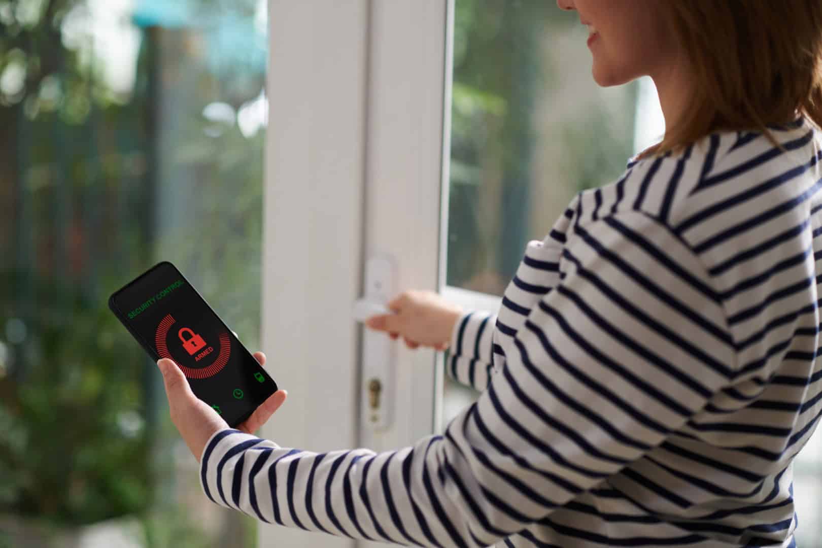 Smiling woman setting home security system with help of mobile application